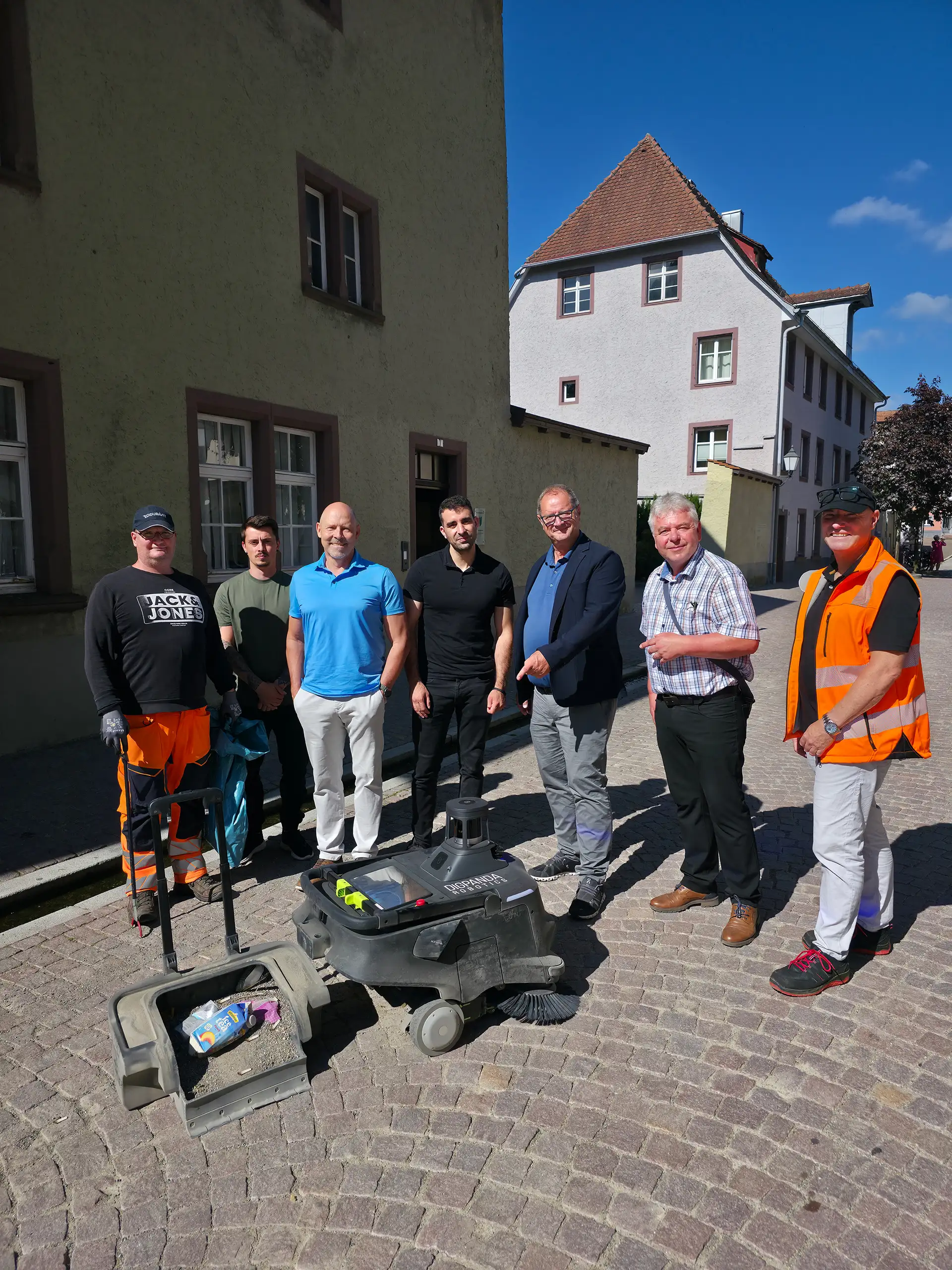 Eine Gruppe von Personen untersucht einen Kehr-/Saugroboter.
