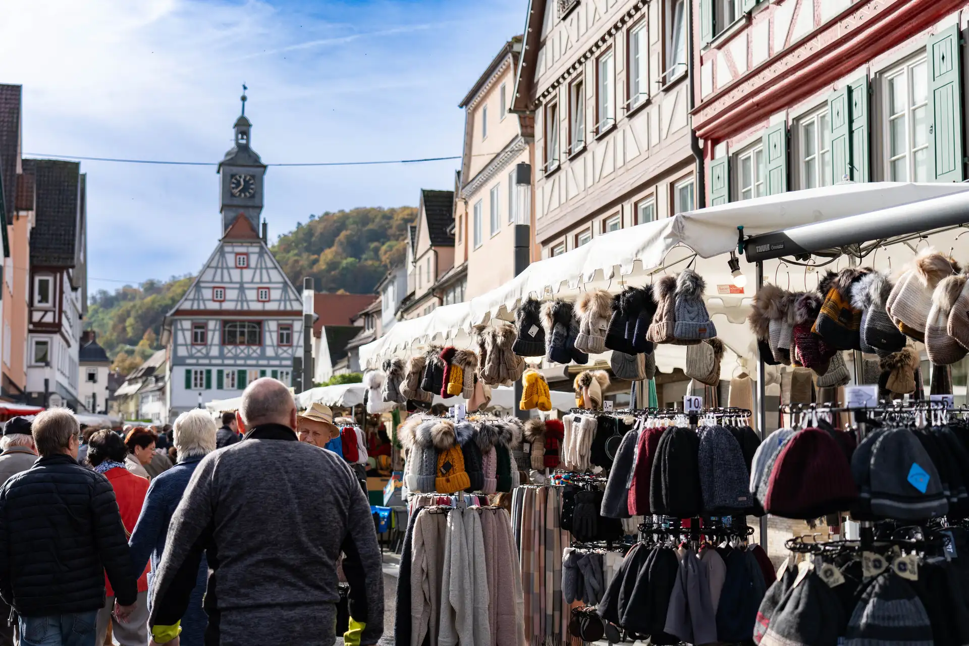 Besucher gehen an Marktständen mit Mützen, Schals und Kleidung in der Künzelsauer Innenstadt vorbei.
