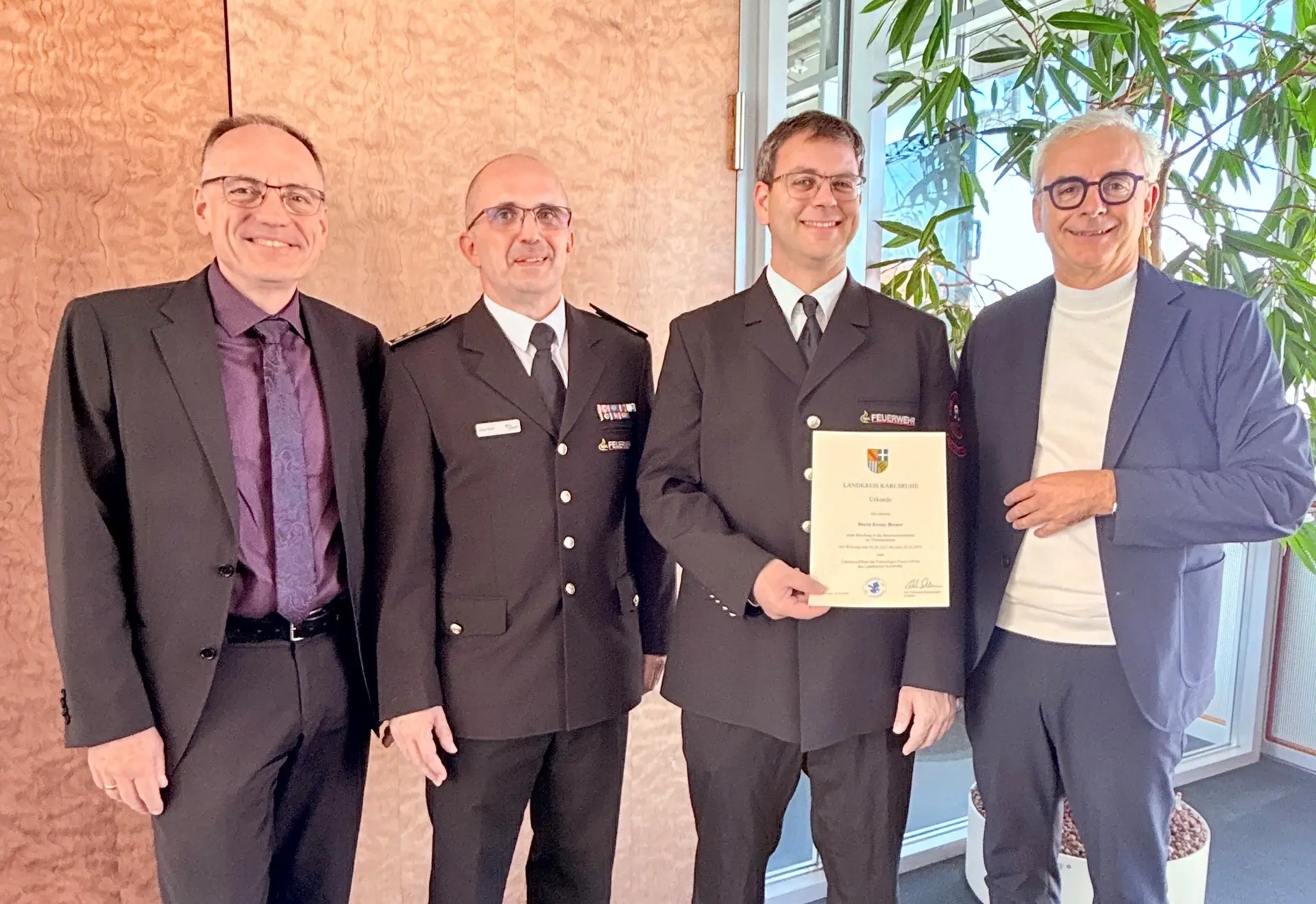 Vier Männer stehen bei einer Urkundenübergabe nebeneinander.
